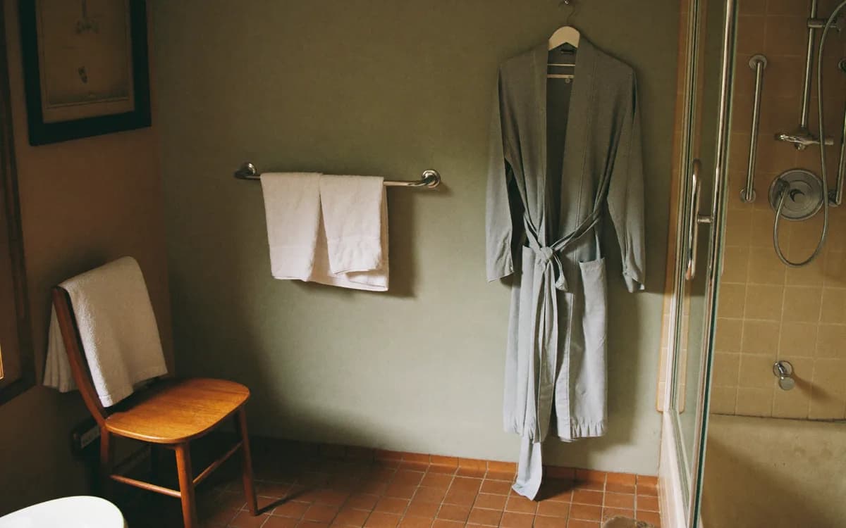 A caregiver lays out fresh towels and a robe beside a bathroom with a shower chair and grab bars